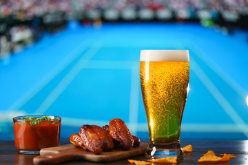 Spicy barbecue chicken wings, tomato salsa, nachos and beer on dark wooden bar table. Football on background, high resolution