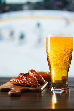 Spicy barbecue chicken wings, tomato salsa, nachos and beer on dark wooden bar table. Hockey on background, high resolution