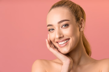 Attractive Woman Touching Face Smiling To Camera Over Pink Background - obrazy, fototapety, plakaty