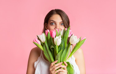 Playful young woman covering face with bouquet of tulips