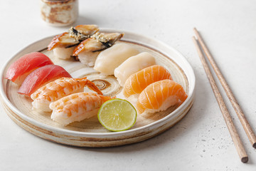 Set of sushi and maki on plate with soy sauce and chopsticks on white background. Top view with copy space