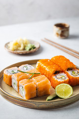 Set of sushi and maki on plate with soy sauce and chopsticks on white background. Top view with copy space