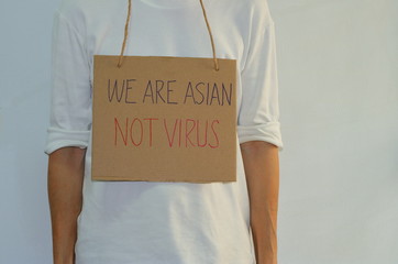 An asian hanging cardboard sign contains handwriting message read WE ARE ASIAN, NOT VIRUS, anti racism concept 