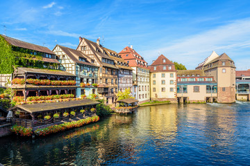 Fototapeta na wymiar Typical half-timbered buildings and former water mills with pastel facades lining the river Ill in the Petite France quarter in Strasbourg, France, on a sunny morning.
