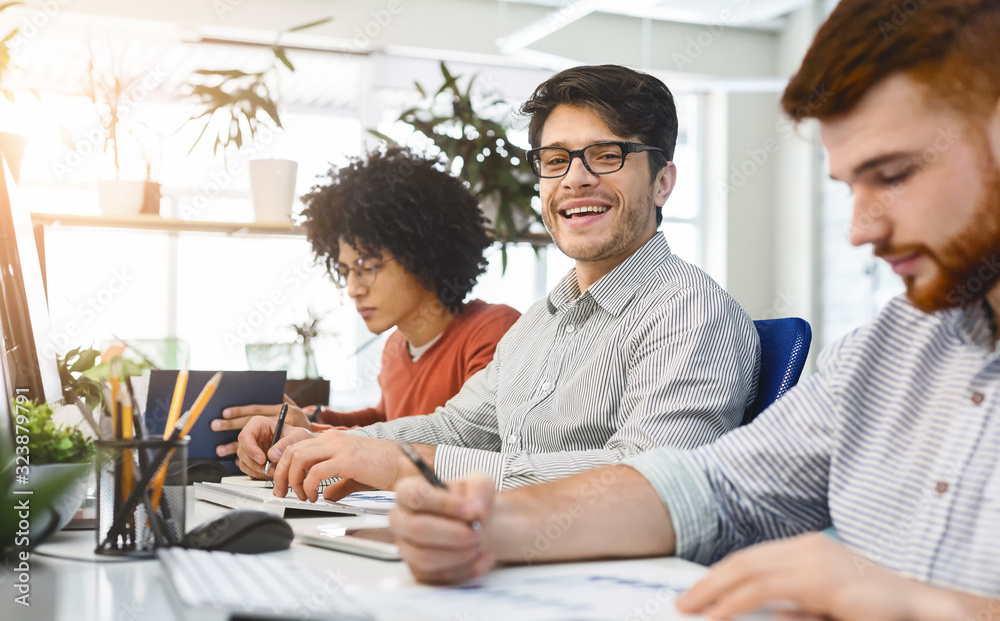 Poster smiling handsome man working in front of laptop with colleagues