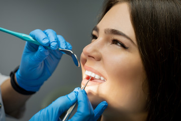 smiling happy brunette woman patient examined by dentist in blue gloves using dental mirror and...
