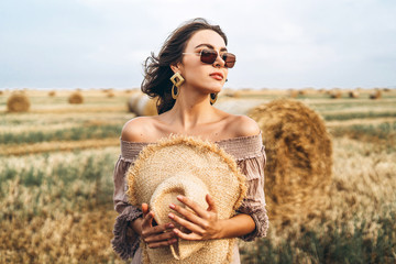 Smiling woman in sunglasses with bare shoulders on a background of wheat field and bales of hay