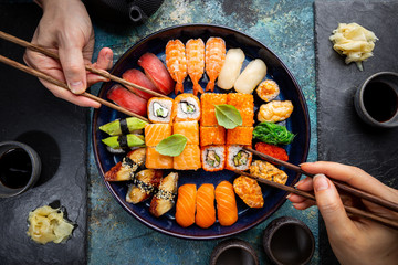 Set of sushi and maki with soy sauce with human hands over blue background. Top view with copy space