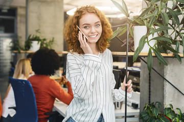 Cheerful redhead girl having conversation on phone in office