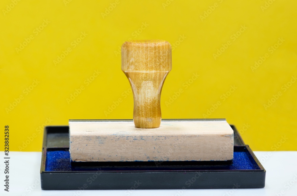 Wall mural rubber stamp with handle on ink pad with blue ink. yellow background with copy space, office concept