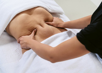 Obraz na płótnie Canvas Masseur pulls hand the skin on the abdomen, showing the body fat in the abdominal area and sides. Treatment and disposal of excess weight, the deposition of subcutaneous fat.