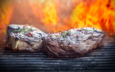Juicy beef rib eye steaks on the grill with rosemary salt spices and flames