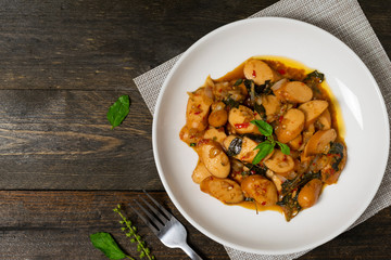 Fried basil with sausages in white dish on the old wooden table.