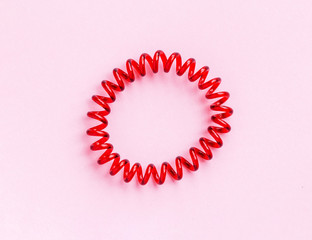 Red spiral rubber bands for hair on a pink background close-up