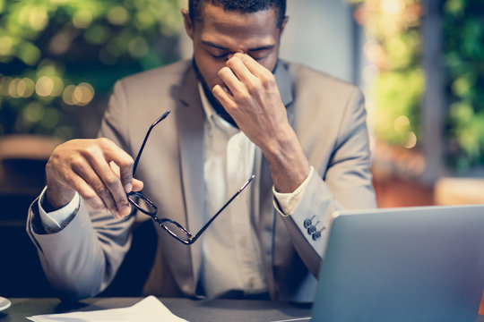 Exhausted afro manager massaging nose sitting at cafe