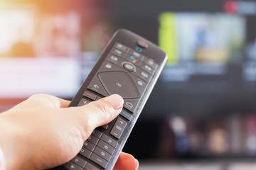 Close-up of woman's hand holding remote control in front of TV,
