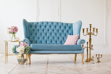 White living room with elegant blue classic sofa with golden candles and flowers. Royal light room....