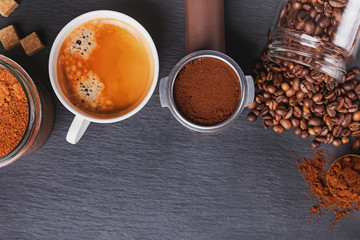 Black coffee, filter holder of espresso maker and scattered roasted coffee beans