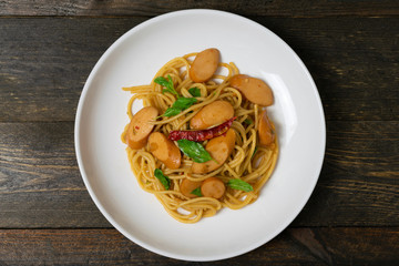 Spaghetti with sausages and fried basil in white dish on the old wooden table.