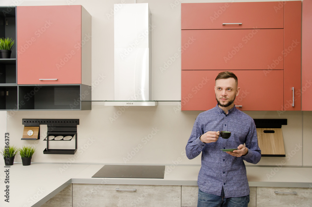 Sticker Attractive bearded man standing drinks coffee in a modern kitchen