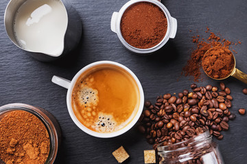 A cup of black coffee, filter holder of espresso maker and scattered roasted coffee beans