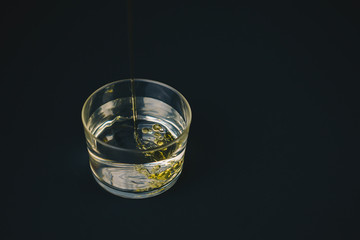 Olive oil falling on water in a low glass with drops of oil on the bottom. Isolated on a black background.Abstract concept,can't be mixed