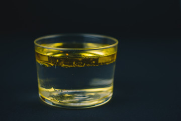 Glass cup with water and oil inside, water and oil perfectly separated. Isolated on a black background.Abstract concept.Copy space