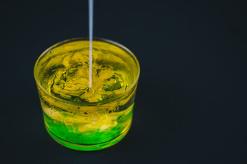 White soap falling on green soap and olive oil in a low glass. Isolated on a black background.Abstract concept.Copy space