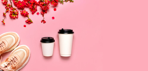 Female Fashionable Sneakers, Coffee or tea paper cup and spring branches of red flowers on pink background top view flat lay. Take away coffee cup, mockup. Creative spring background, lifestyle