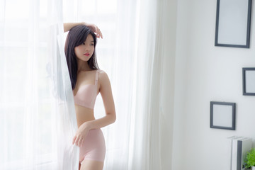 Obraz na płótnie Canvas Beautiful portrait young asian woman sexy standing the window and smile while wake up with health, body of girl happy with freshness and cheerful with wellbeing, lifestyle and relax concept.