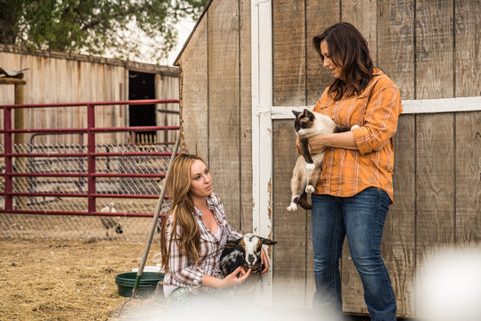 Young farmgirl and mother holding goat and cat. Bridger, Montana, USA