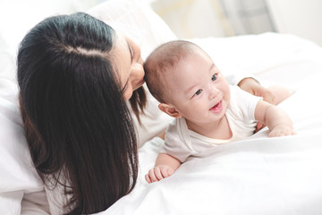 Mother playing with her baby daughter on the bed. The daughter is happy and laughing