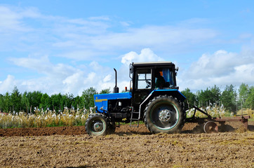 Blue tractor in a field of land plowing. Mechanization of tillage and crop planting. Loosening and preparing the land for sowing grain, cultivation. Agriculture Concept - Image