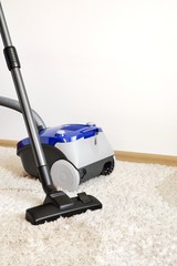 Canister modern vacuum cleaner blue for cleaning the house on the background of a soft beige...