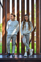 A young girl and a young man in the same clothes on a wooden bench.