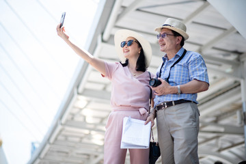 A elder couple is taking selfies while traveling abroad.