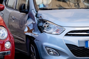 A small blue hatchback damaged in a car accident with a broken headlamp and fender waiting for...