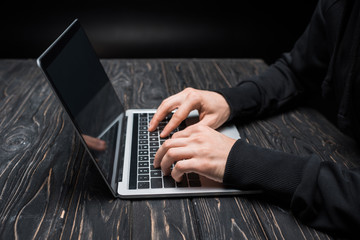 cropped view of hacker typing on laptop keyboard on black