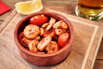 Shrimp stew in a stew pan with tomatoes, spice and beer served on a wooden table