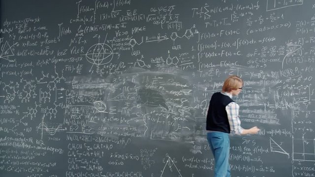 Time lapse of intelligent guy in glasses writing scientific formulas on chalkboard at school busy with education. Modern people, lifestyle and youth concept.