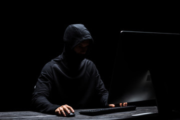 hooded anonymous hacker in mask using computer isolated on black