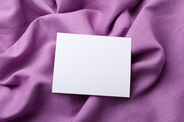 Closeup of empty white cardboard on the violet linen fabric.Blank paper card for text and information
