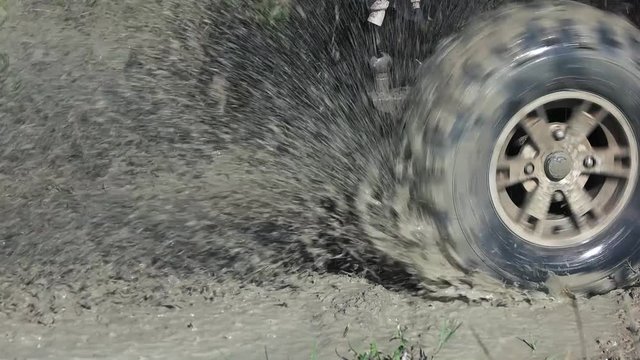 Spinning offroad wheel splashing dirt water. Close up, slow motion.