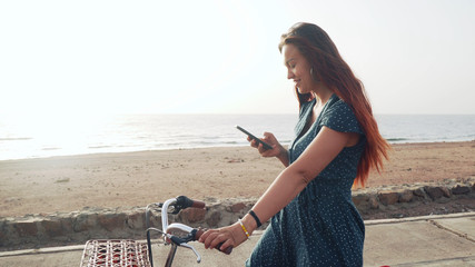 Handsome red hair female using her smartphone standig with bicycle at sea