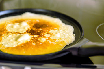 pancake frying pan with crepe pancake cooking on cooker in kitchen