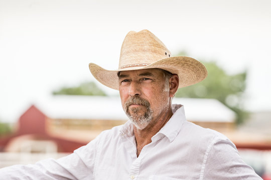 Portrait of cowboy with cowboy hat standing at fence on his ranch. Bridger, Montana, USA