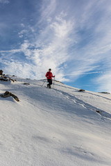 Fototapeta na wymiar Single woman walking uphill, serene winter day in mountain, bright sun shining in the blue sky