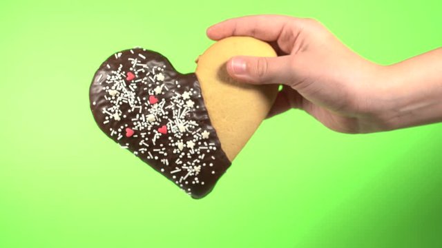Closeup view 4k video of cute small hand of young white kid holding special sweet cookie in shape of heart. Happy Valentine day oy Mothres day holiday celebration concept.