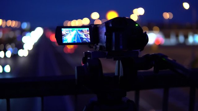 Camera captures another camera that captures cars go by on a highway on a dark night.