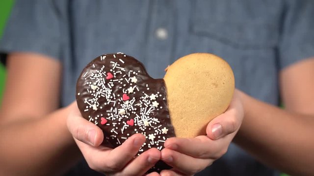 Closeup front view of cute small hands of young white kid holding special sweet cookie in shape of heart. Happy Valentine day oy Mothres day holiday celebration concept.